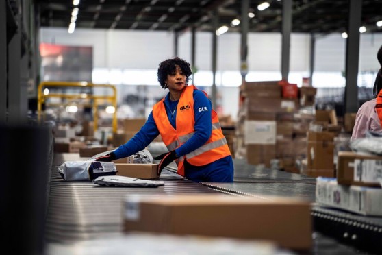 A woman sorting parcels on a conveyor belt in a warehouse.